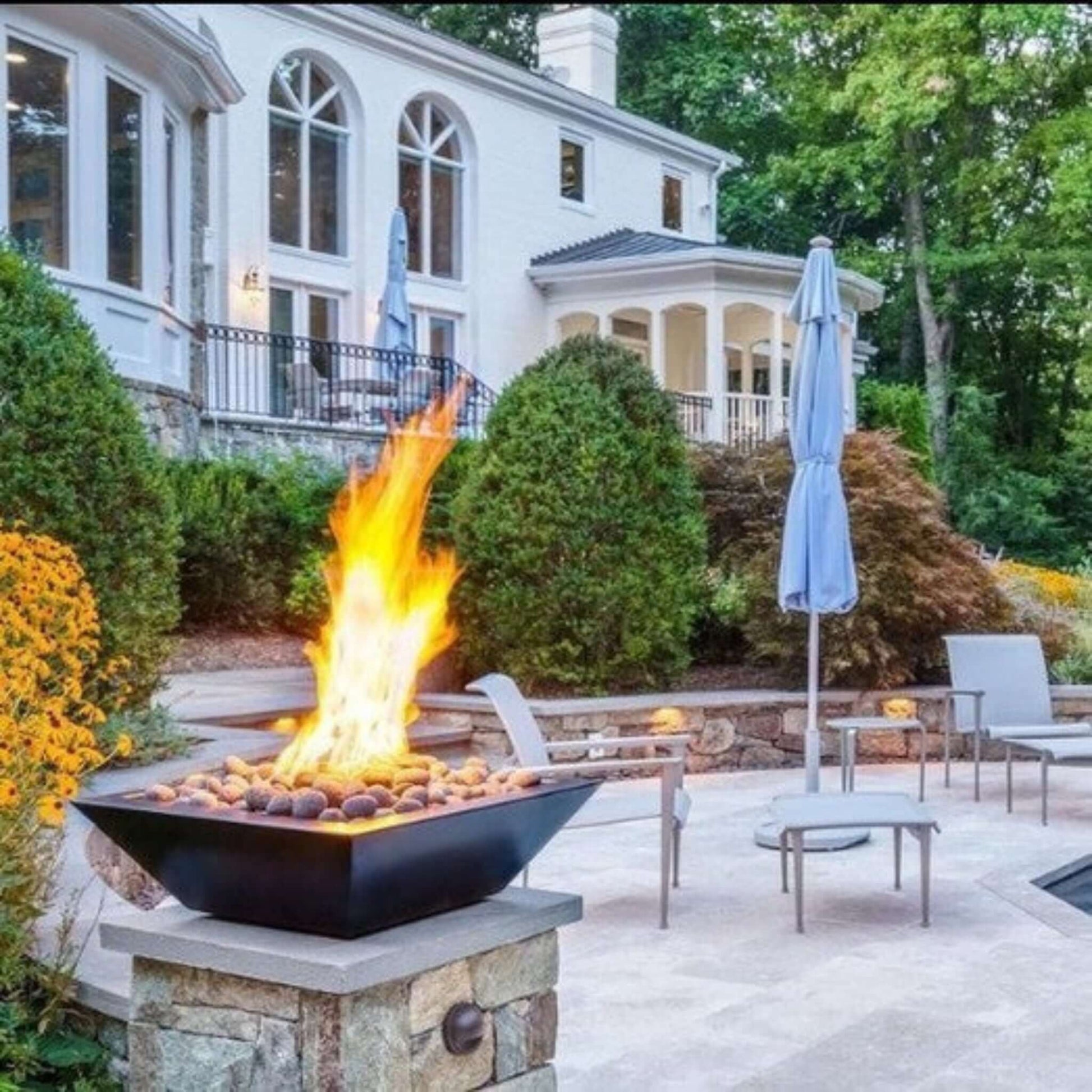 Outdoor scene featuring Grand Effects Corinthian Fire Bowl with flames, modern design, and SOS Pool vibes, SKU: GF30C.
