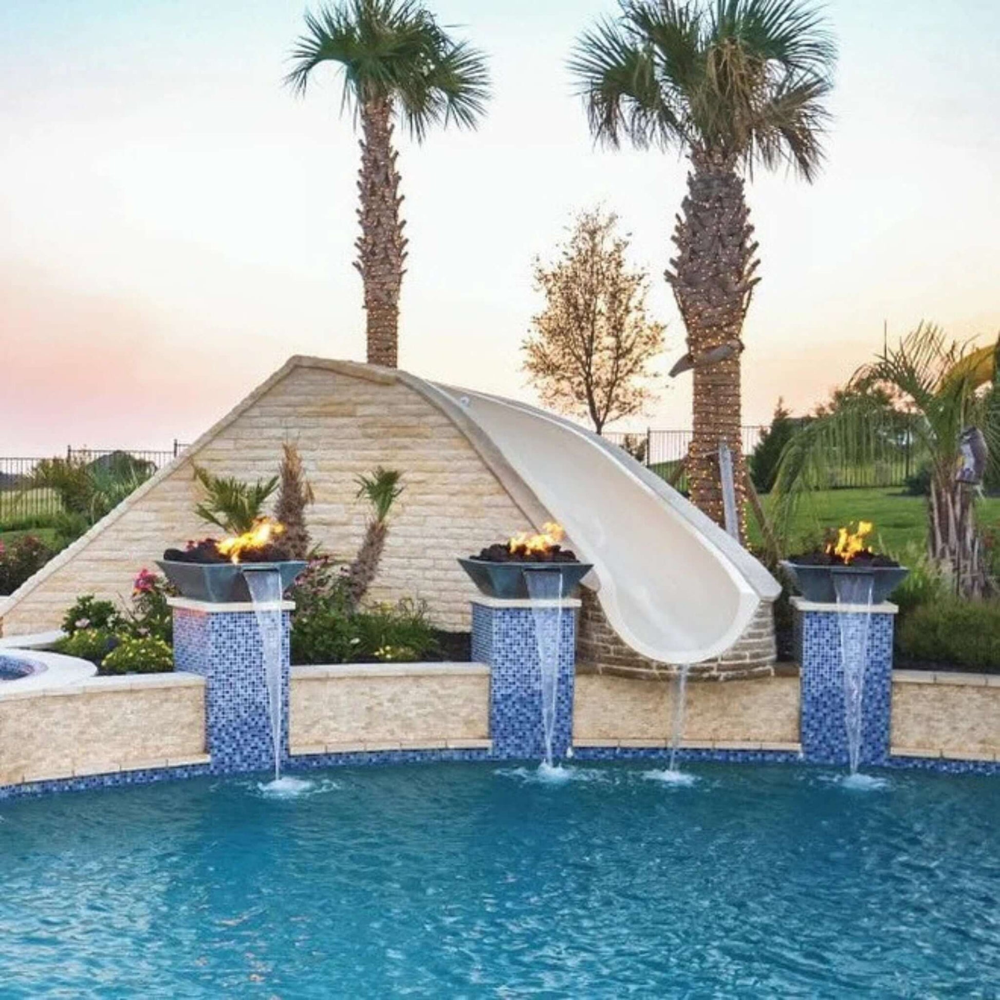 Stunning pool scene featuring a waterslide and fire features, surrounded by palm trees and vibrant landscaping.