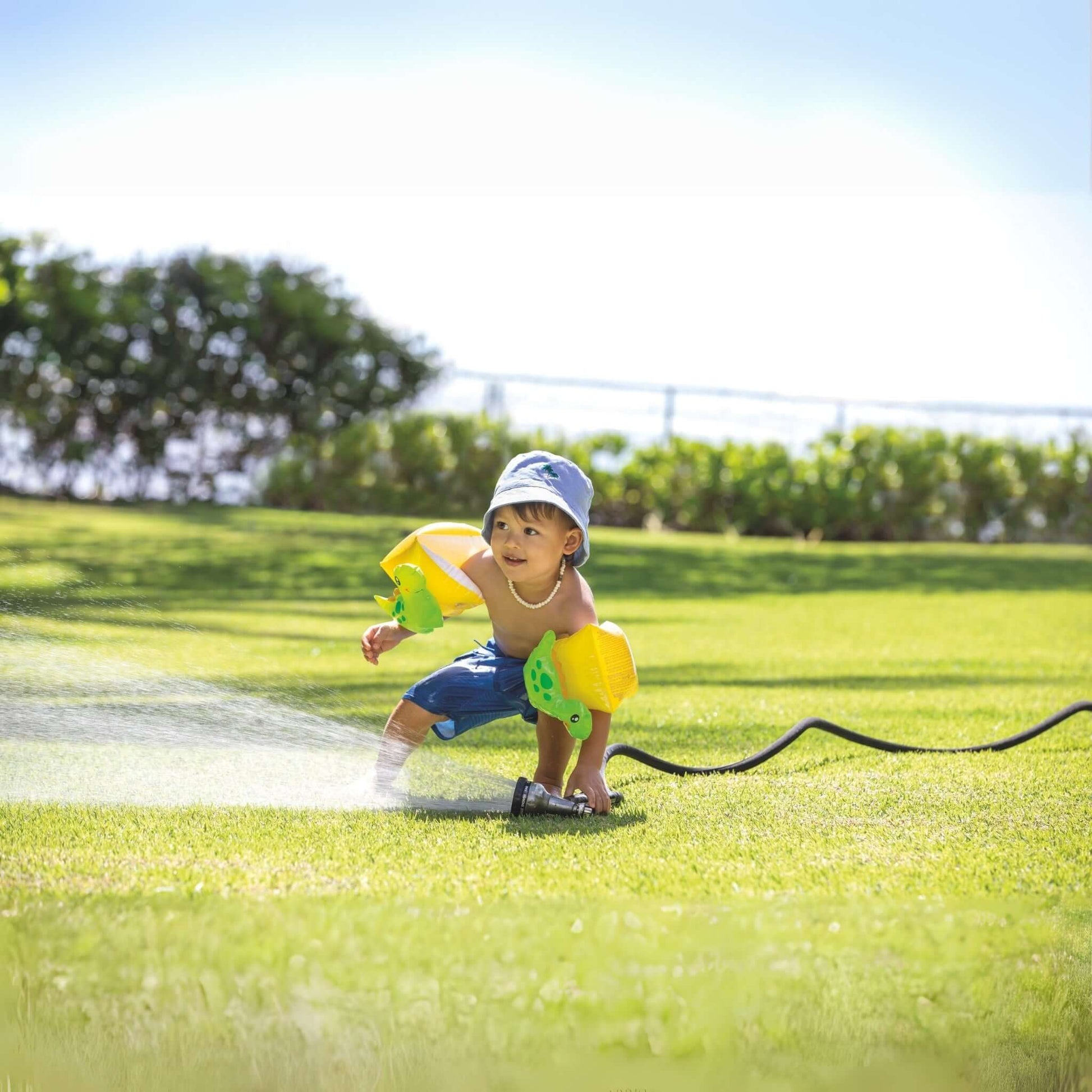 Child wearing Intex Dinosaur Arm Bands playing in sprinkler, highlighting SOS Pool safety and fun, SKU 32132J.