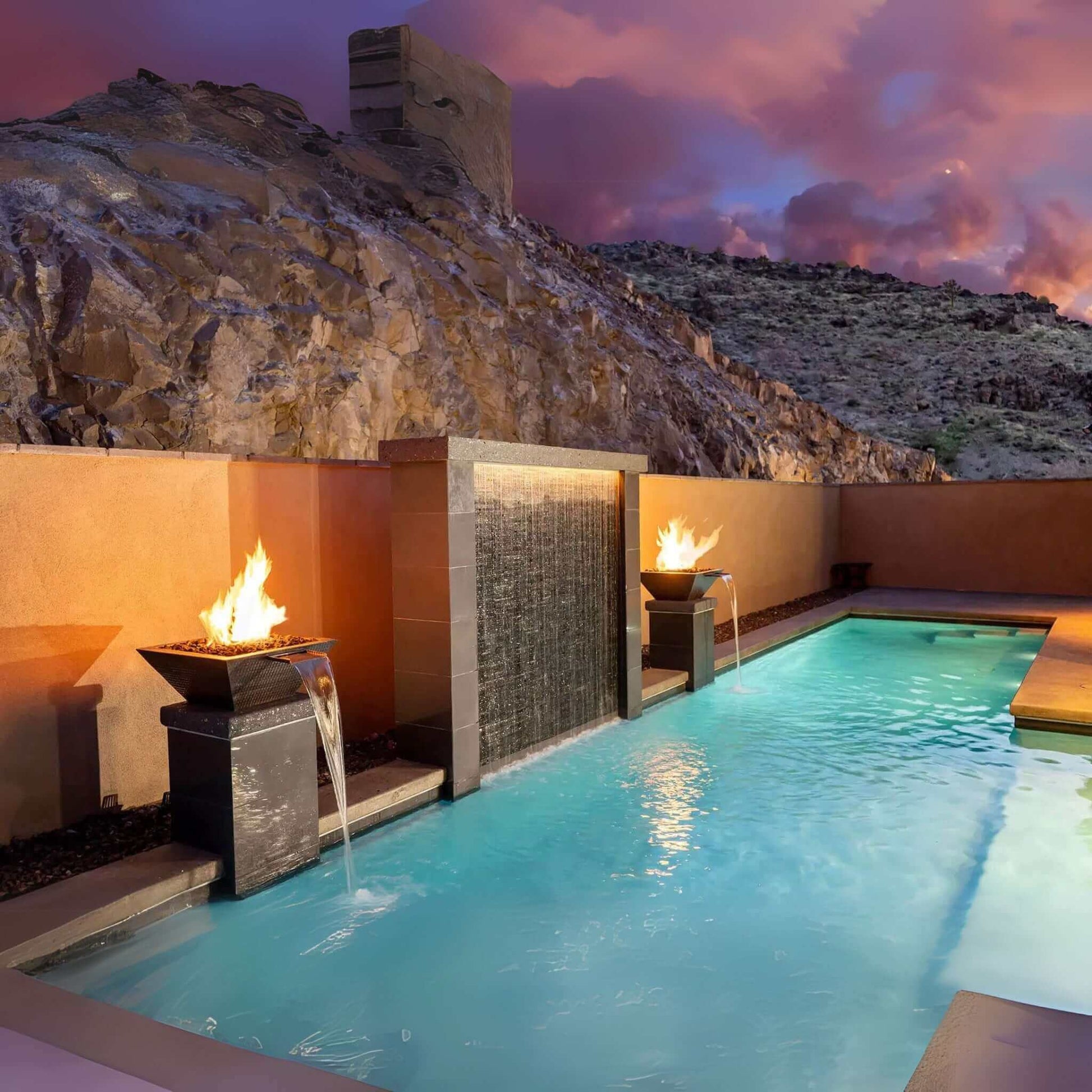 Outdoor pool with fire features in a stunning natural landscape, perfect for luxury relaxation. Discount Pool Mart DPM.