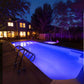 Beautiful outdoor pool lit with vibrant purple lighting at night, surrounded by trees and a cozy house.