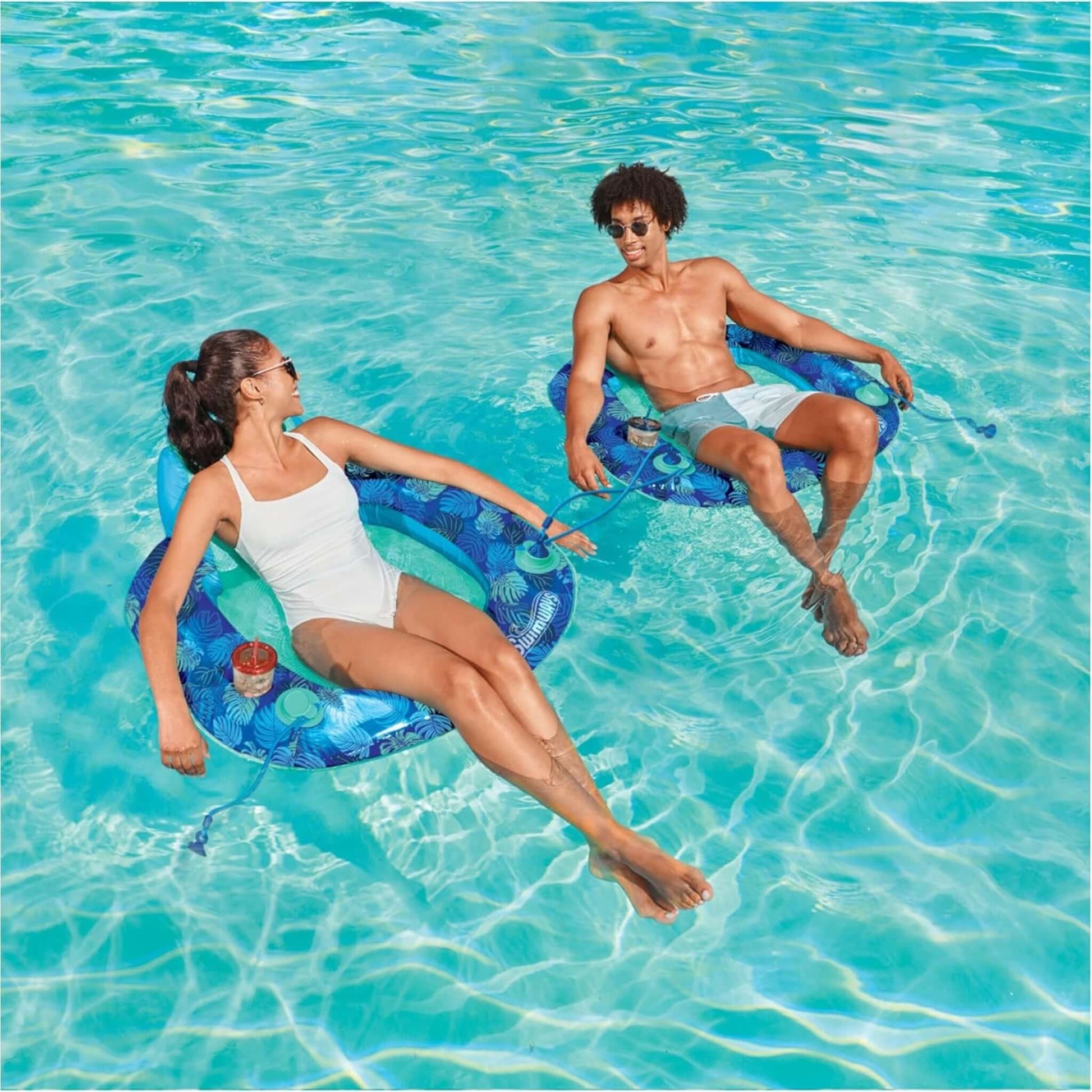 Two people relaxing on SwimWays Elite Spring Float Sunseat in a pool, SKU: 6069309. Enjoying SOS Pool lounging.