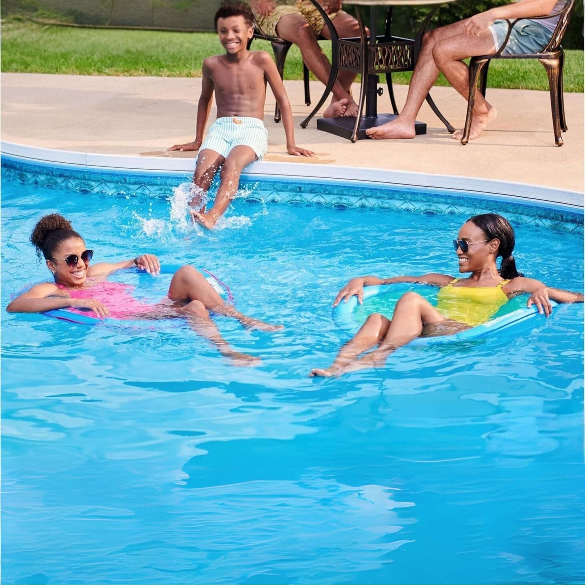 Family enjoying pool time with SwimWays Premium Spring Float Papasan, kids relax on floats while another splashes.