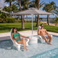 Two people relaxing in TenJam Splash Woosah In-Pool Chairs under an umbrella, enjoying sunny weather by the pool.